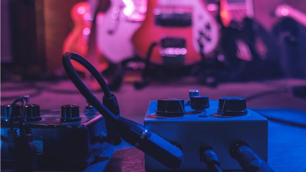 A loop pedal in front of a set of guitars