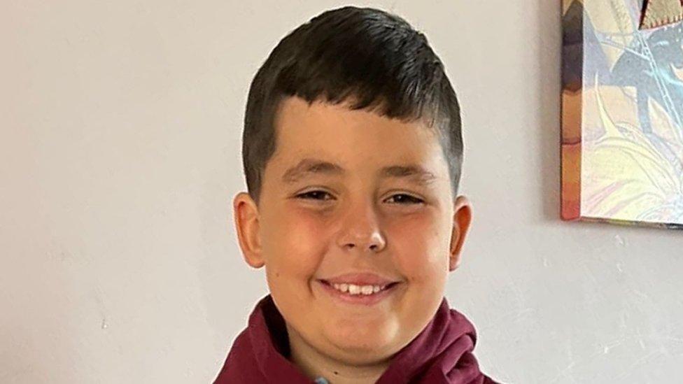 A family photo shows 10-year-old Jack Lis, who was mauled to death by an XL Bully dog. He is smiling broadly, has brown hair, and is wearing a red hooded top.