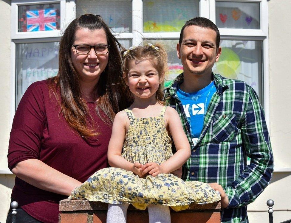 A smiling young girl sitting on her garden wall with her parents