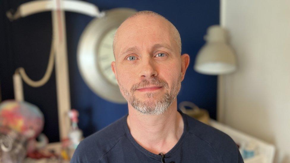 A man with a shaved head and greying beard looking at camera