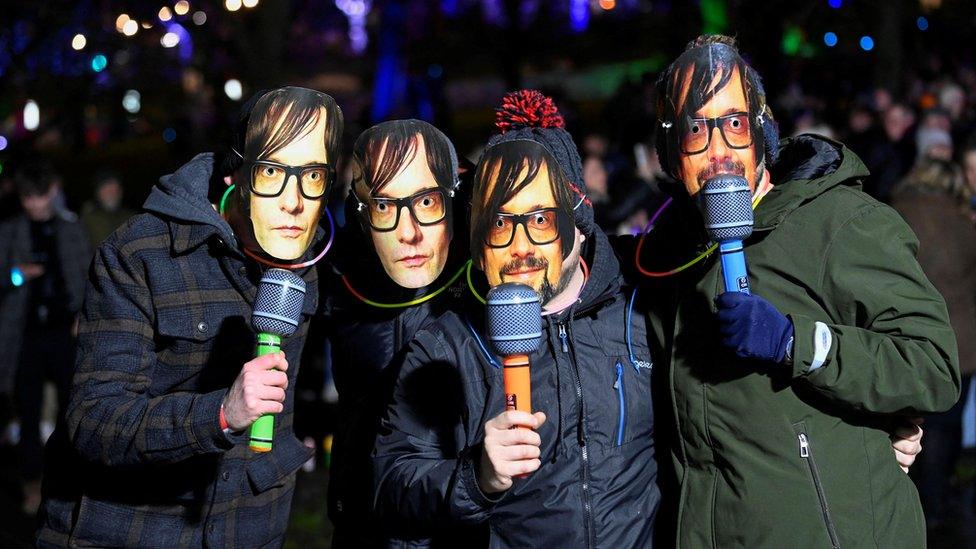 Four people wearing Jarvis Cocker masks pose