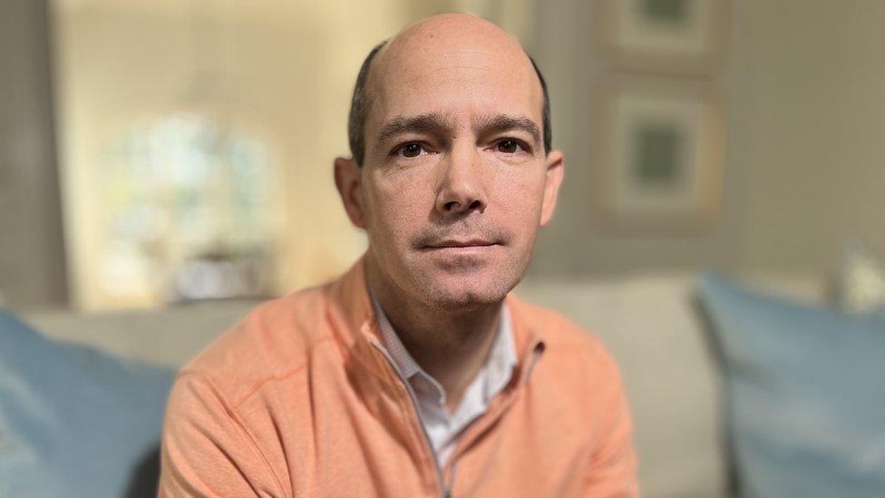 Rodney Miller wearing a white shirt and orange pullover