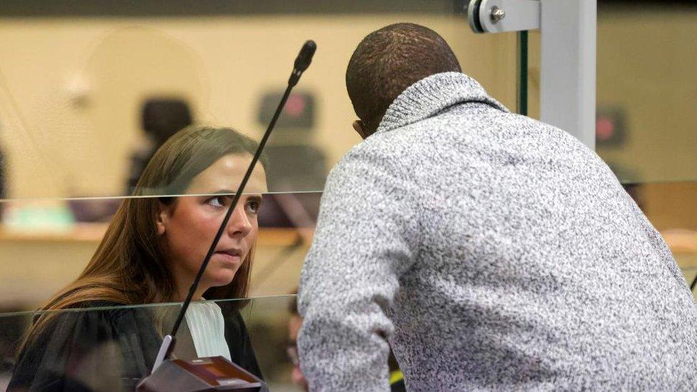 A barrister speaks to a defendant through a glass shield