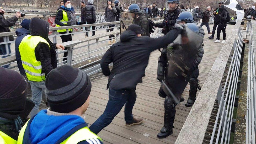 A man in a boxing stance fights riot police during a demonstration by "Gilets Jaunes" anti-government protesters on a bridge leading to the National Assembly in Paris on January 5, 2019