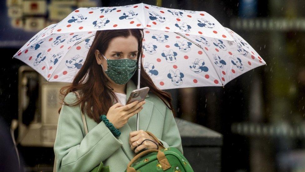 A woman walking in Belfast city centre underneath an umbrella wearing a face mask