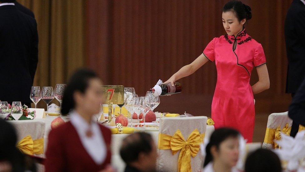 A waitress pours a bottle of wine at a banquet