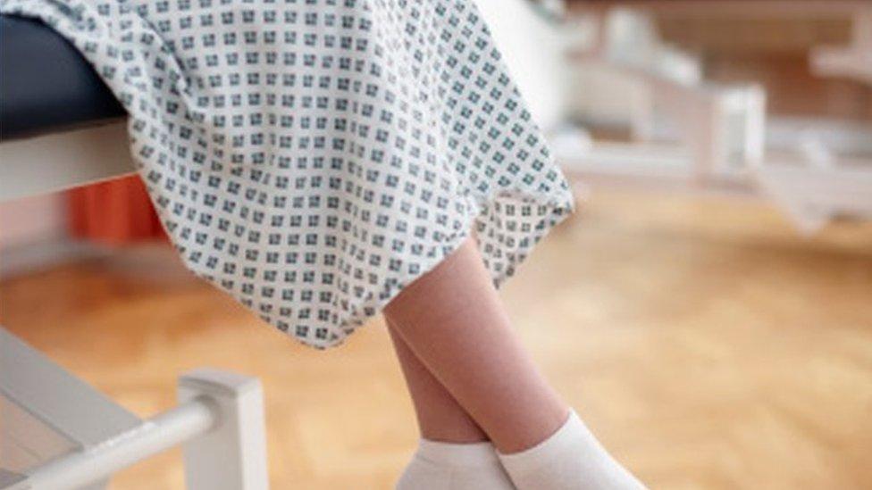 Woman sitting on hospital bed, wearing examination gown