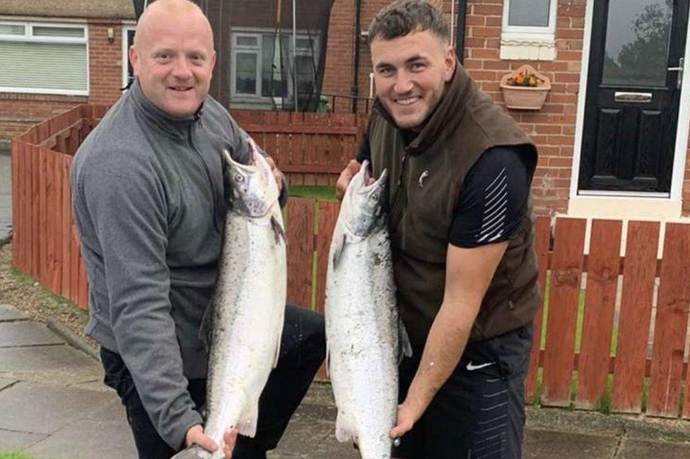 Two men each holding a large fish up to camera