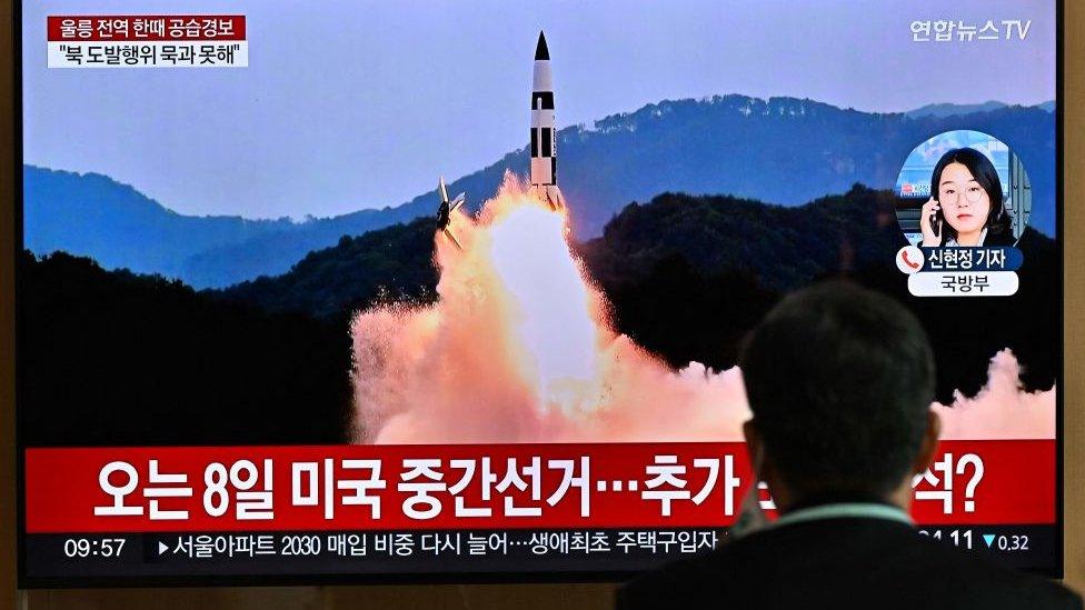 A man watches a television screen showing a news broadcast with file footage of a North Korean missile test