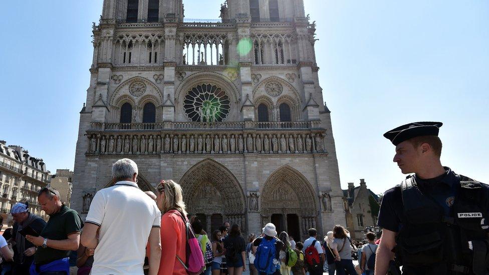 A French police officer stands guard by Notre Dame Cathedral in Paris as people queue for the mass for the feast of the Assumption on August 15, 2016.