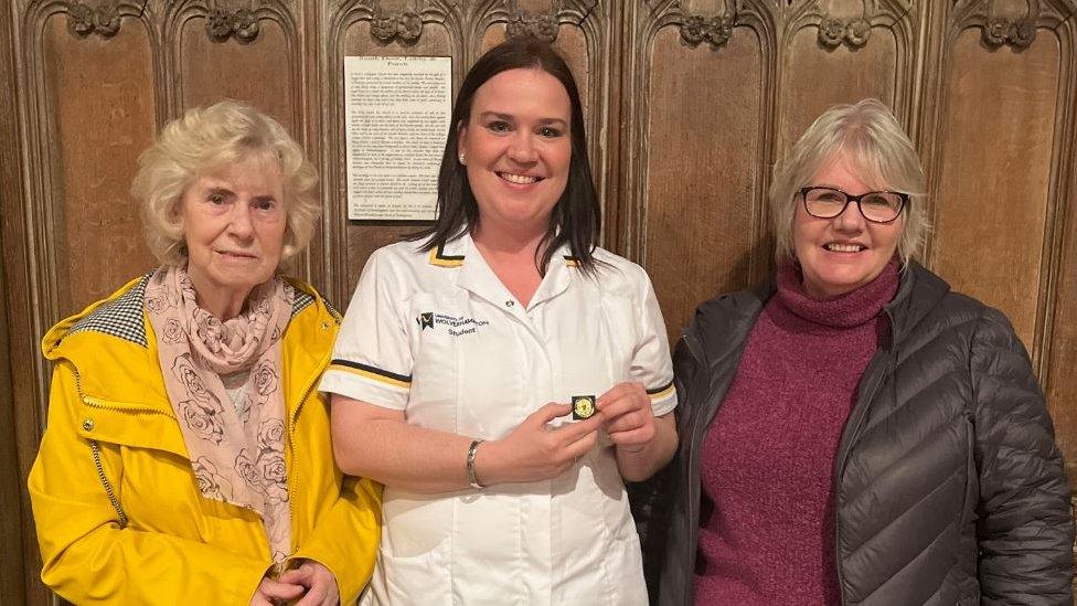 A nurse holding a badge standing in between her mother and grandmother