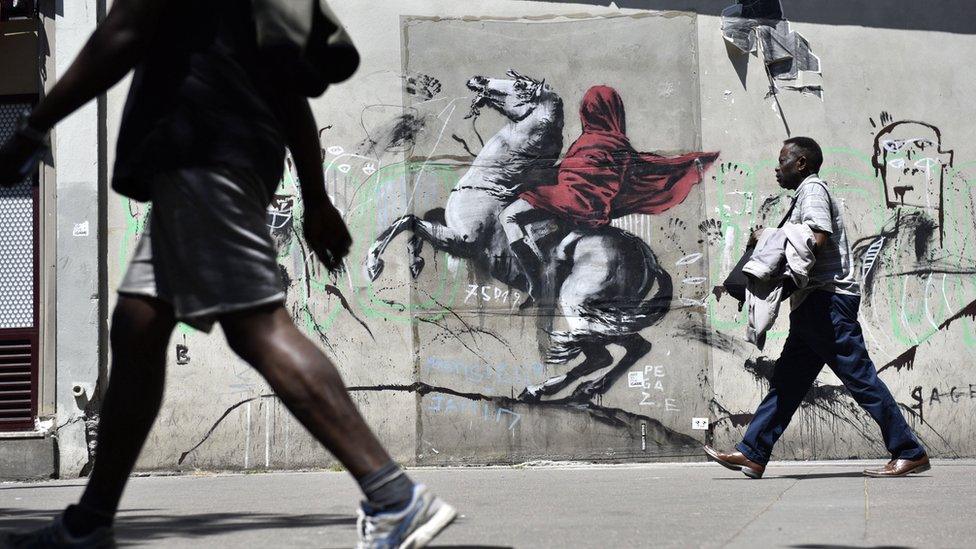 People walk by a recent artwork believed to be attributed to Banksy showing Napoleon rearing his horse, wrapped in a red cloak in the 19th district of Paris