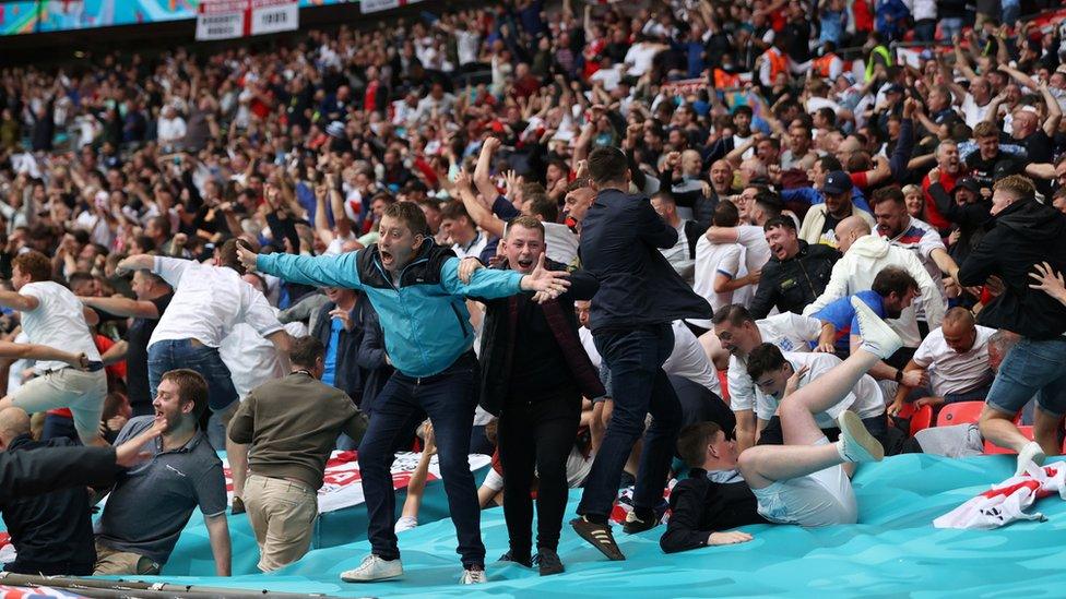 Fans tumble over the tarpaulin at Wembley after Raheem Sterling's opener