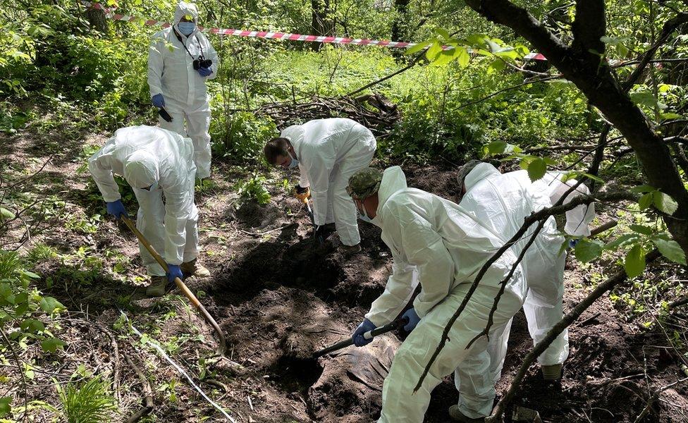 A Ukrainian forensic team remove a Russian soldier from a shallow grave on the outskirts of Kyiv