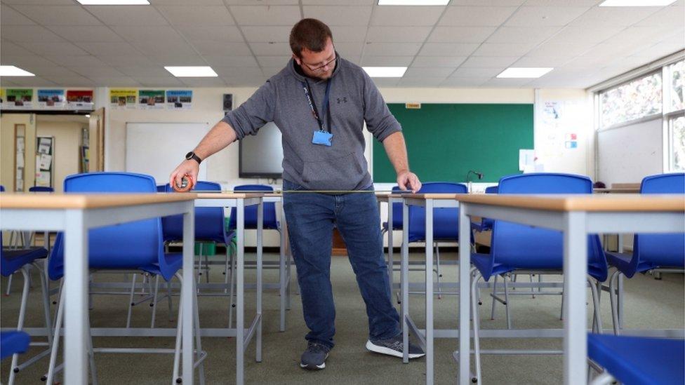 A school caretaker ensures desks are properly spaced