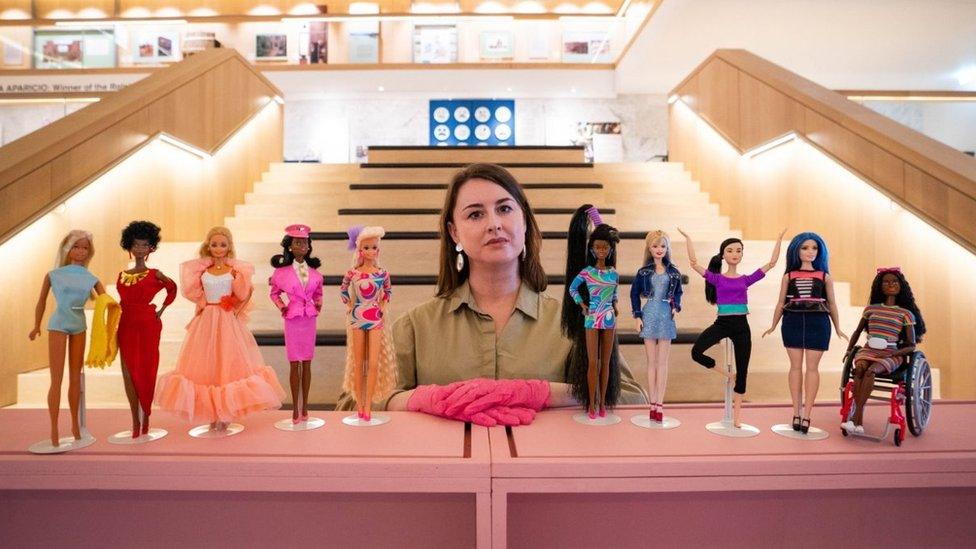 Danielle Thom standing in the middle of a row of diverse Barbies from various decades