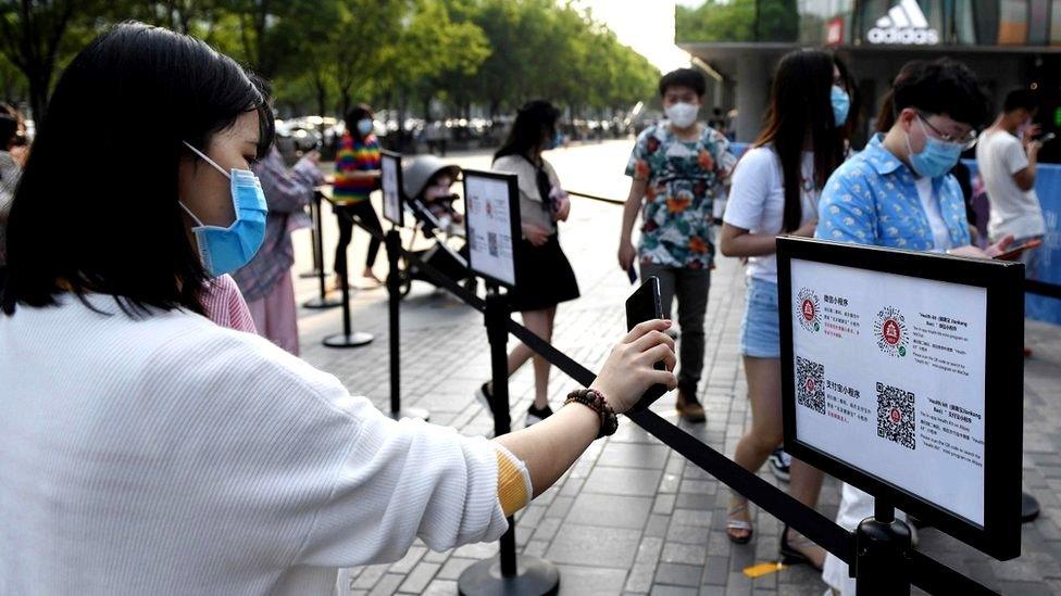 A woman holds her phone to a QR code to validate that she has not been registered as carrying Covid or should be in isolation