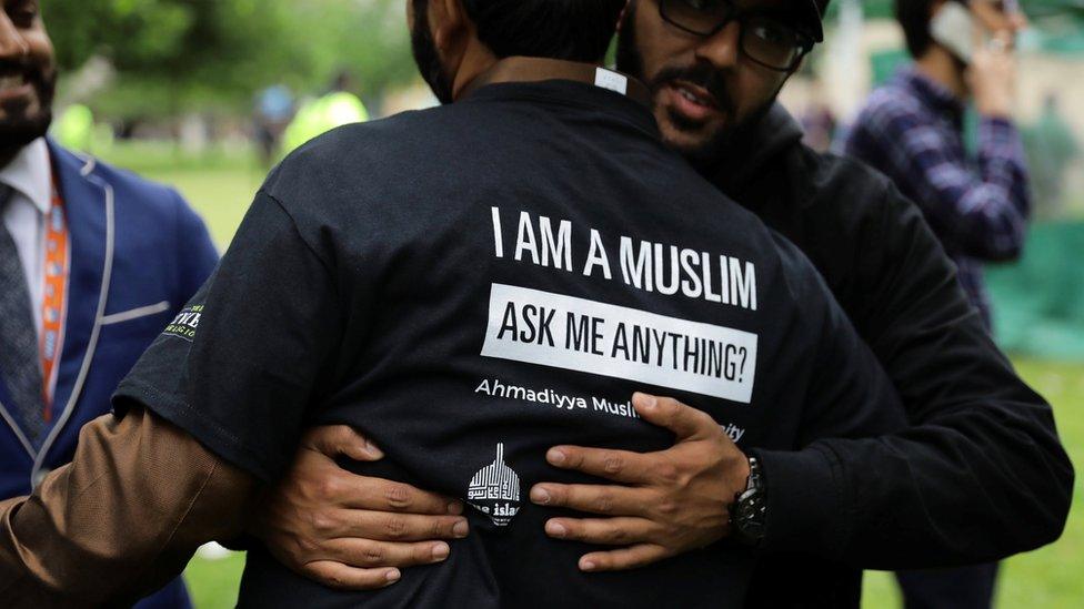 A man hugs another man, wearing a t-shirt saying "I am a Muslim, ask me anything?"