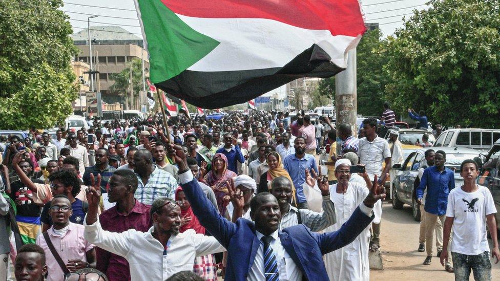 A man flashes the victory gesture while waving a Sudanese national flag during a mass demonstration