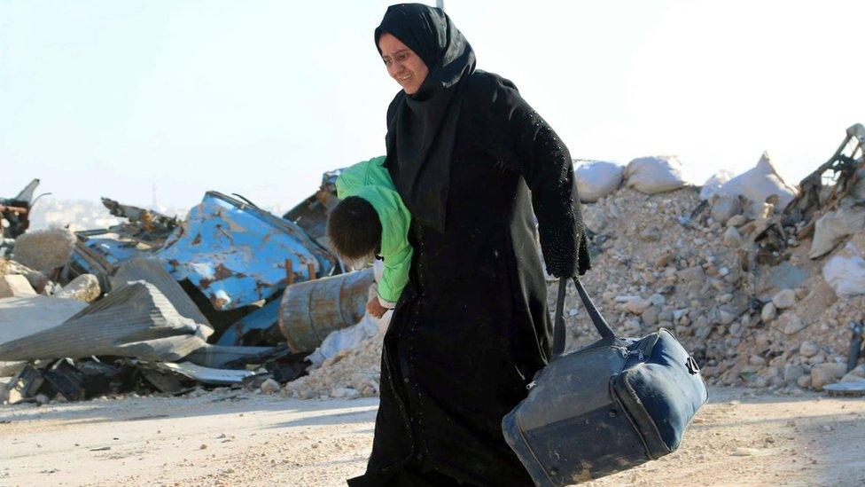 A Syrian woman carries her child in one hand and a bag in the other, as she flees rebel-held eastern neighbourhoods of Aleppo into the Sheikh Maqsoud area that is controlled by Kurdish fighters (photo provided by The Rumaf) (27 November 2016)