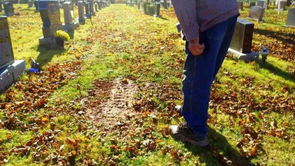 Mr Kickham points to the earth where his grave has been dug out, and recovered ahead of the funeral