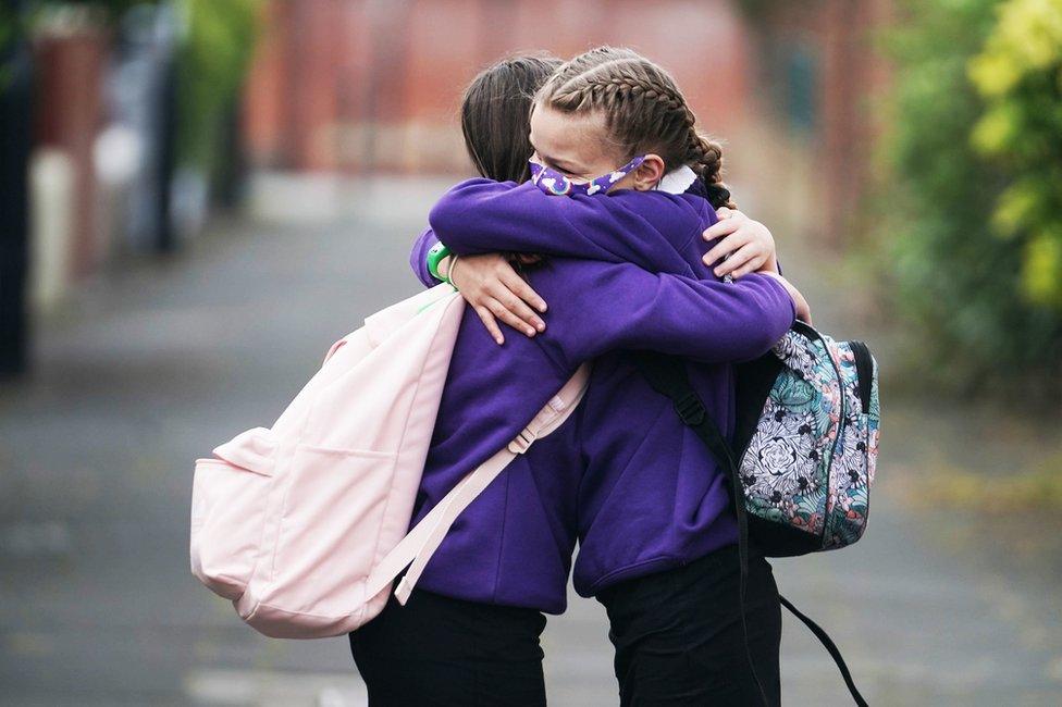 Two grils wearing masks embrace each other