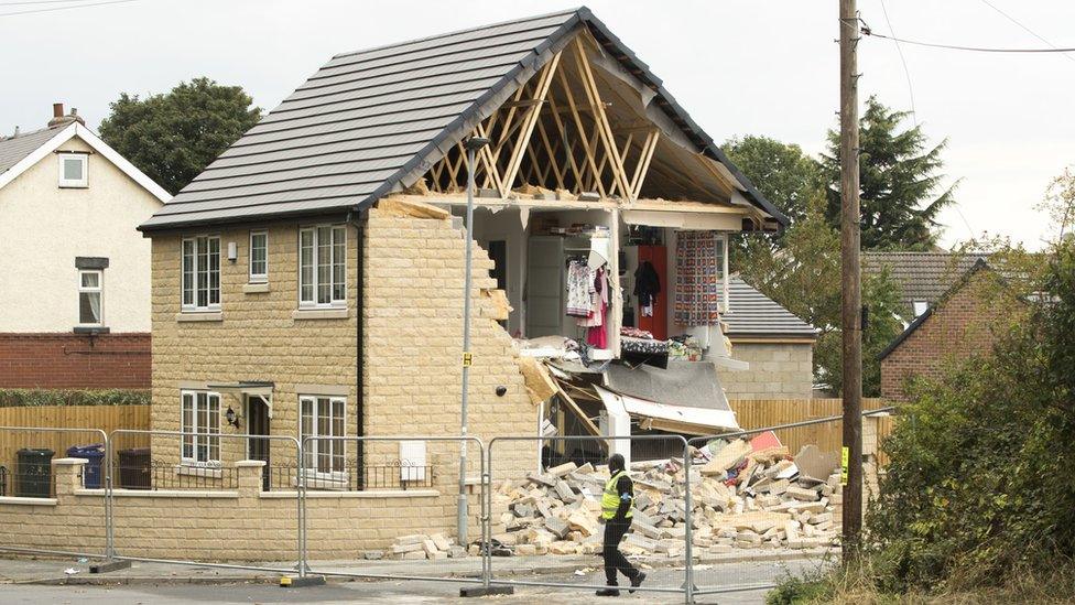 Damaged house with side of the property exposed showing clothes and contents; rubble on the ground outside