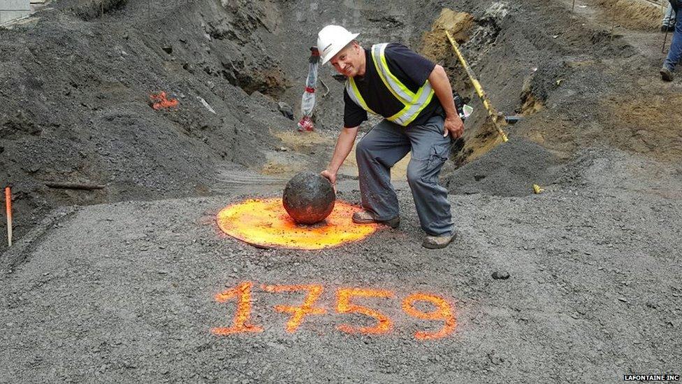 A worker poses beside the cannonball in Quebec