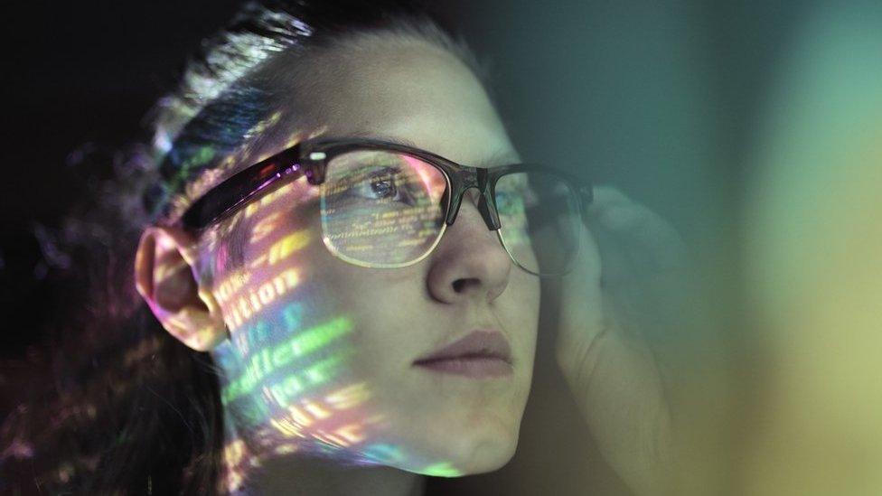 A woman's face is lit up with strings of code