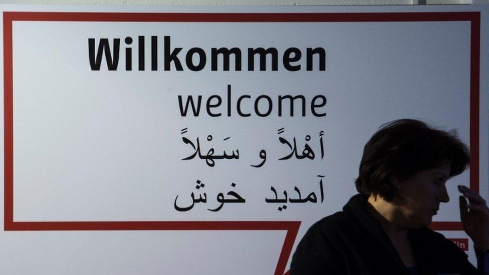 A volunteer stands in front of a sign reading "Welcome" in German, English, Farsi and Arabic during the inauguration of a new jobs counselling centre for migrants and refugees at the former Tempelhof Airport in Berlin (27 January 2016)