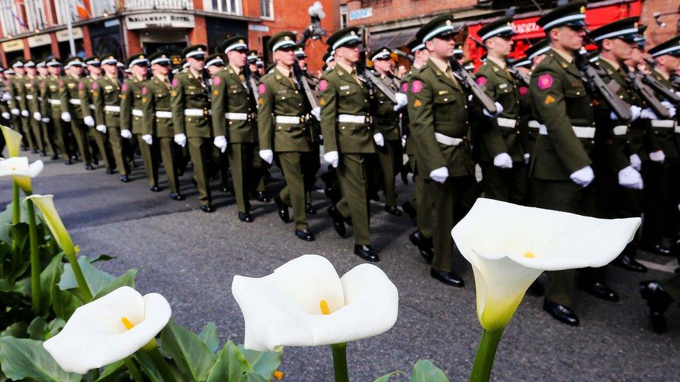 Members of the Irish defence forces walk past white lilies on Dublin's Dame Street