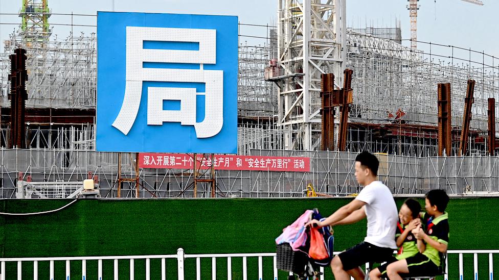 A man and children cycle past the Guangzhou FC football stadium, which is being built by Evergrande.