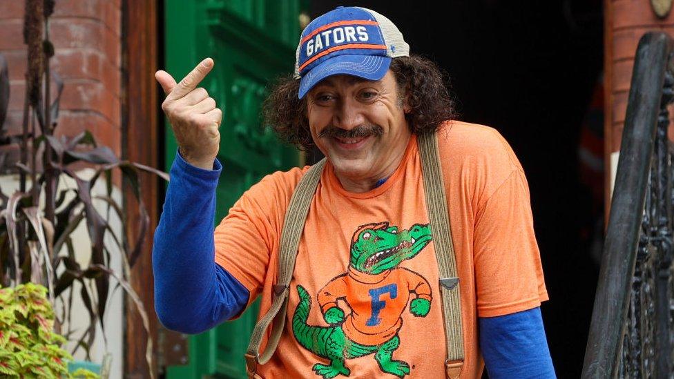 javier bardem posing while wearing a crocodile t shirt and gators baseball cap