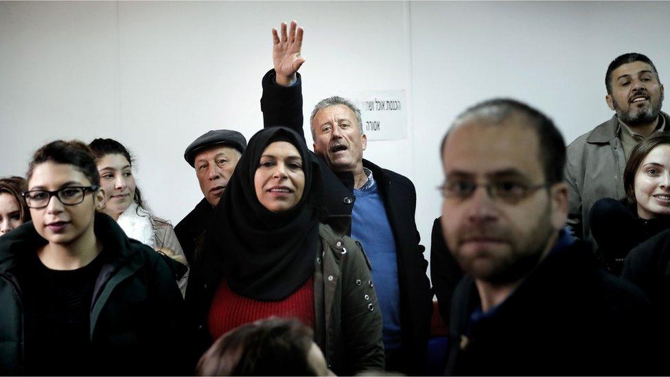 Basseem Tamimi, Ahed's father, waves to her from the back of a crowded court room when she arrives