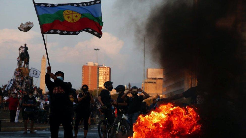 A protester waves a Mapuche flag while walking near a fire during a protest against President Sebastian Piñera on March 5, 2021 in Santiago, Chile.