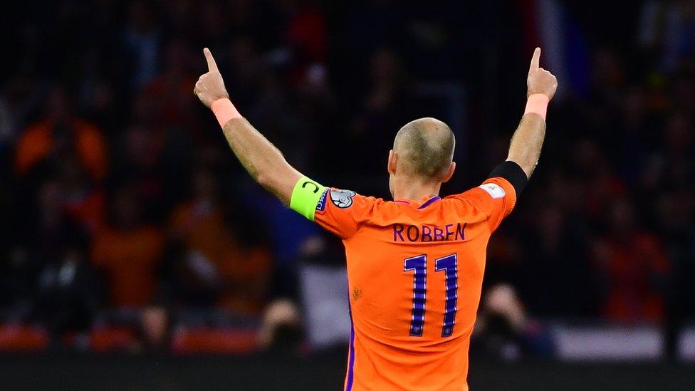 Arjen Robben holds his hands up to a crowd of spectators in a football stadium, wearing his captain armband.