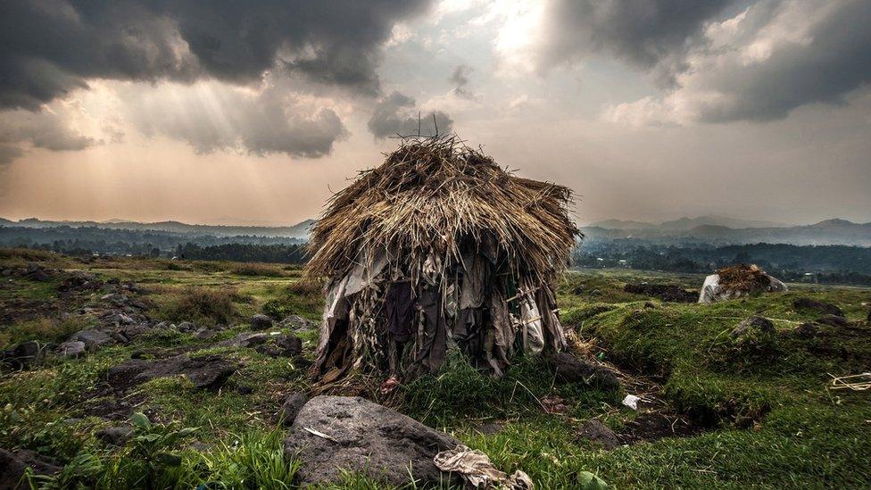 single thatched hut in the middle of a deep green landscape, with broken rays of sunlight breaking through the cloud