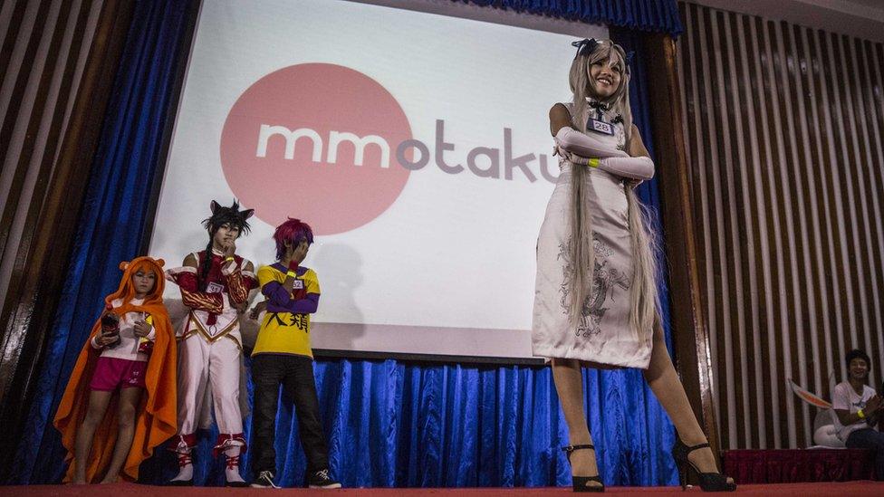 A woman in a cosplay dress stands on stage, in front of three other waiting participants, during the event