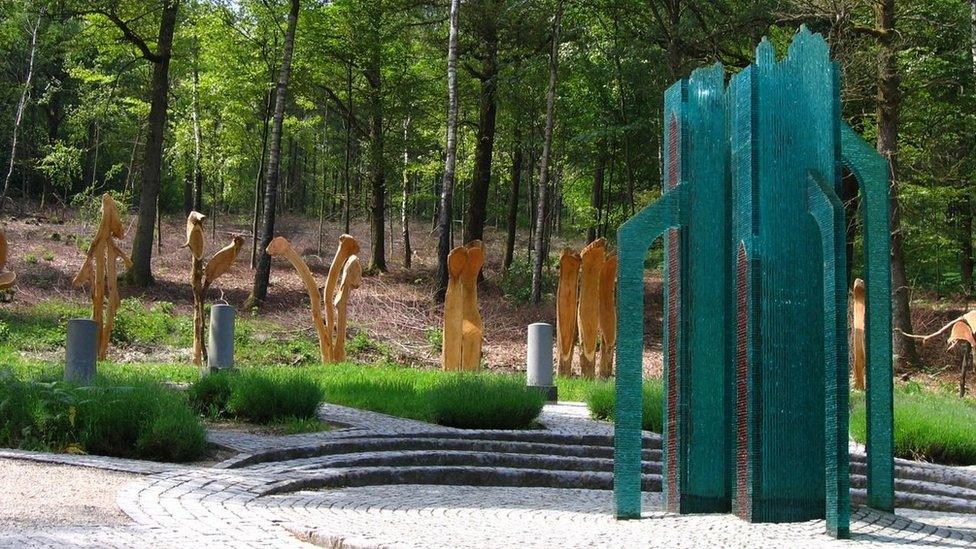 A small green monument located near trees in Viroinval