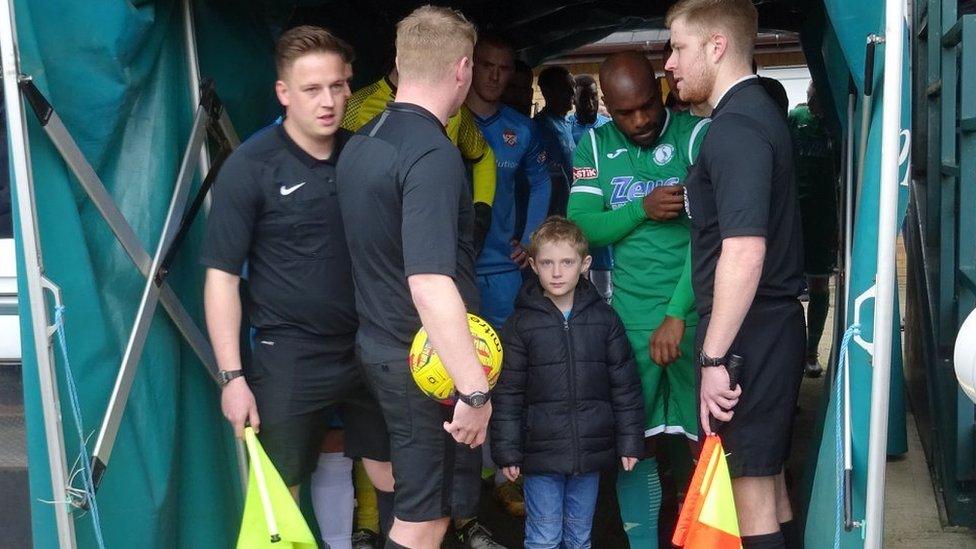 Liam standing in the middle of a tunnel, with football players and referees around him