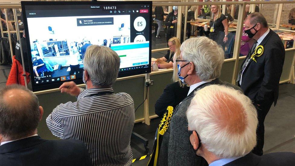 A group of people gather around a screen in Ayr to check spoilt ballots