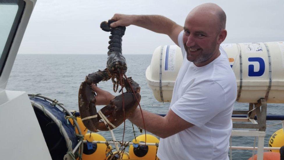 Lewis Mulhearn on a boat holding a lobster