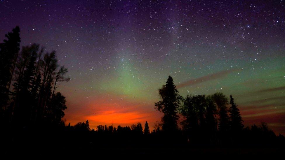 Wildfires glow underneath the Northern Lights, also known as the Aurora Borealis, near Fort McMurray, Alberta (07 May 2016)