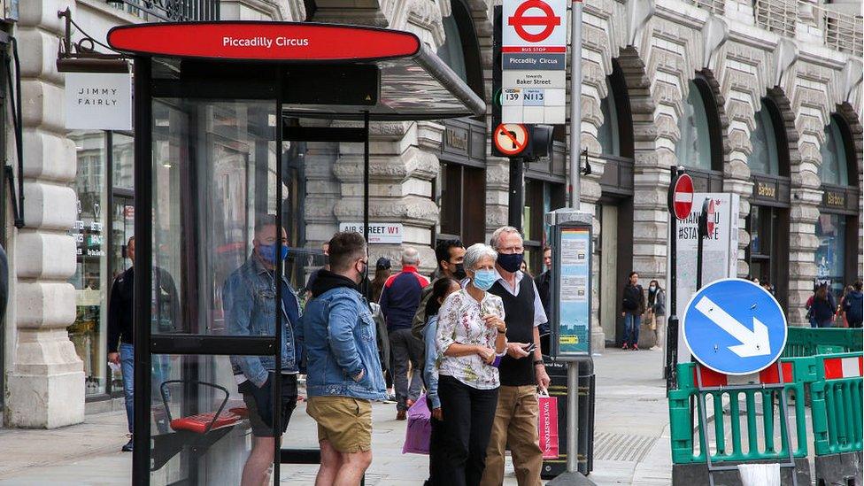 people wearing masks waiting a bus stop