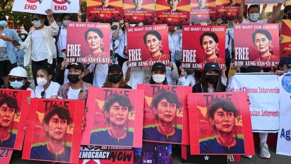 Protesters in Myanmar hold up signs showing jailed leader Aung San Suu Kyi