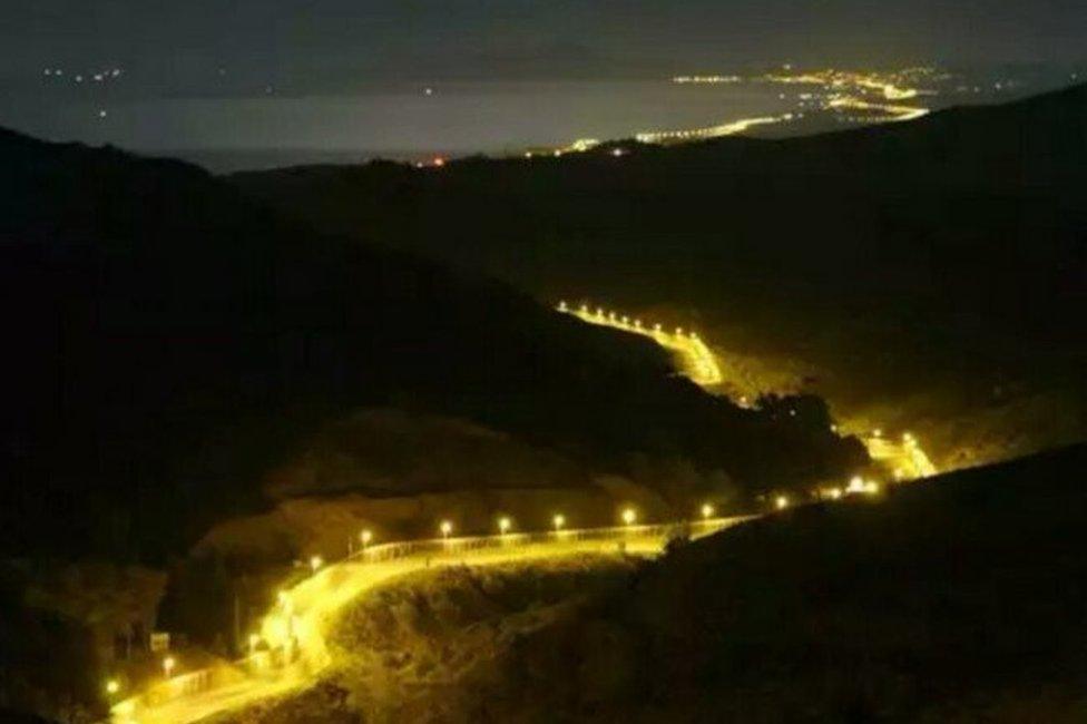 Photo of a well-lit border fence along interlocking hills at night. The picture was taken in Ceuta in 2006