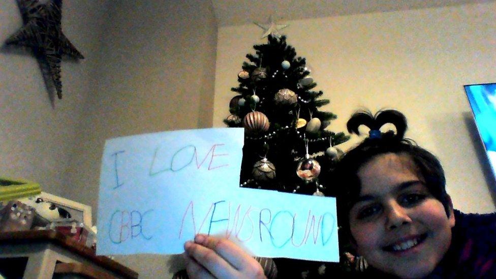 girl in front of tree with sign saying 'i love cbbc newsround'