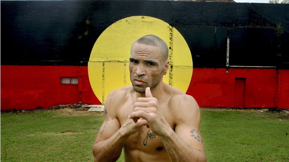 Anthony Mundine in a boxing pose in front of an Aboriginal flag mural