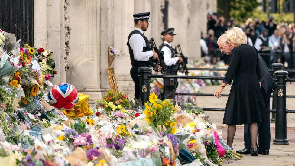 King Charles and Queen Camilla look at flowers outside Buckingham Palace