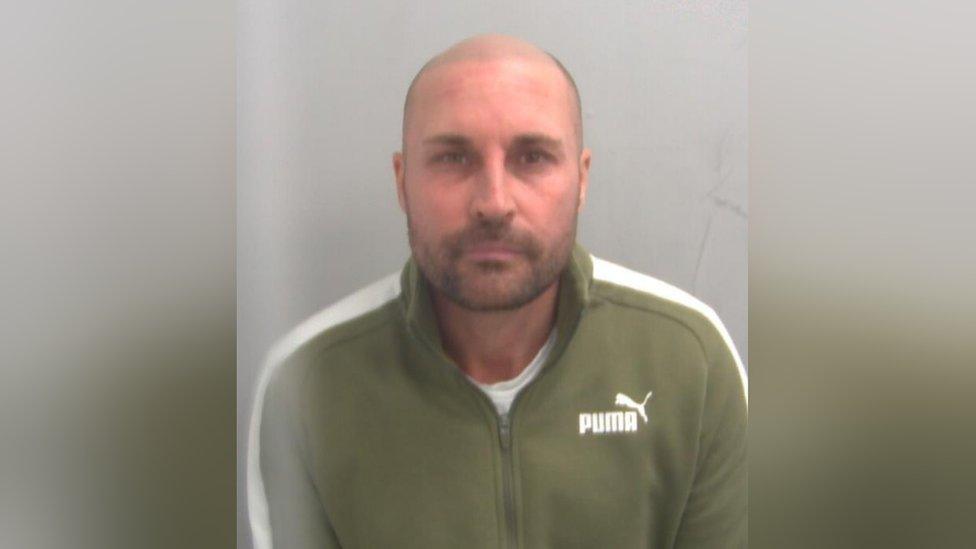 David Richards custody image from Essex Police. He is wearing a green sweater with white stripes on the arms.